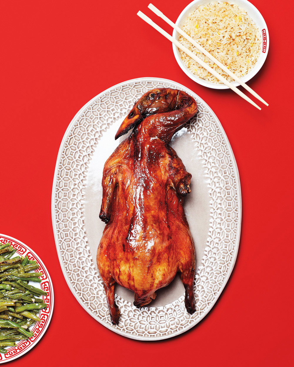 A roasted duck, rice, and green beans on a red tablecloth