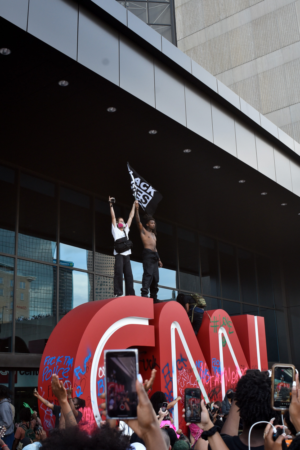 two protestors stand atop CNN sign holding 