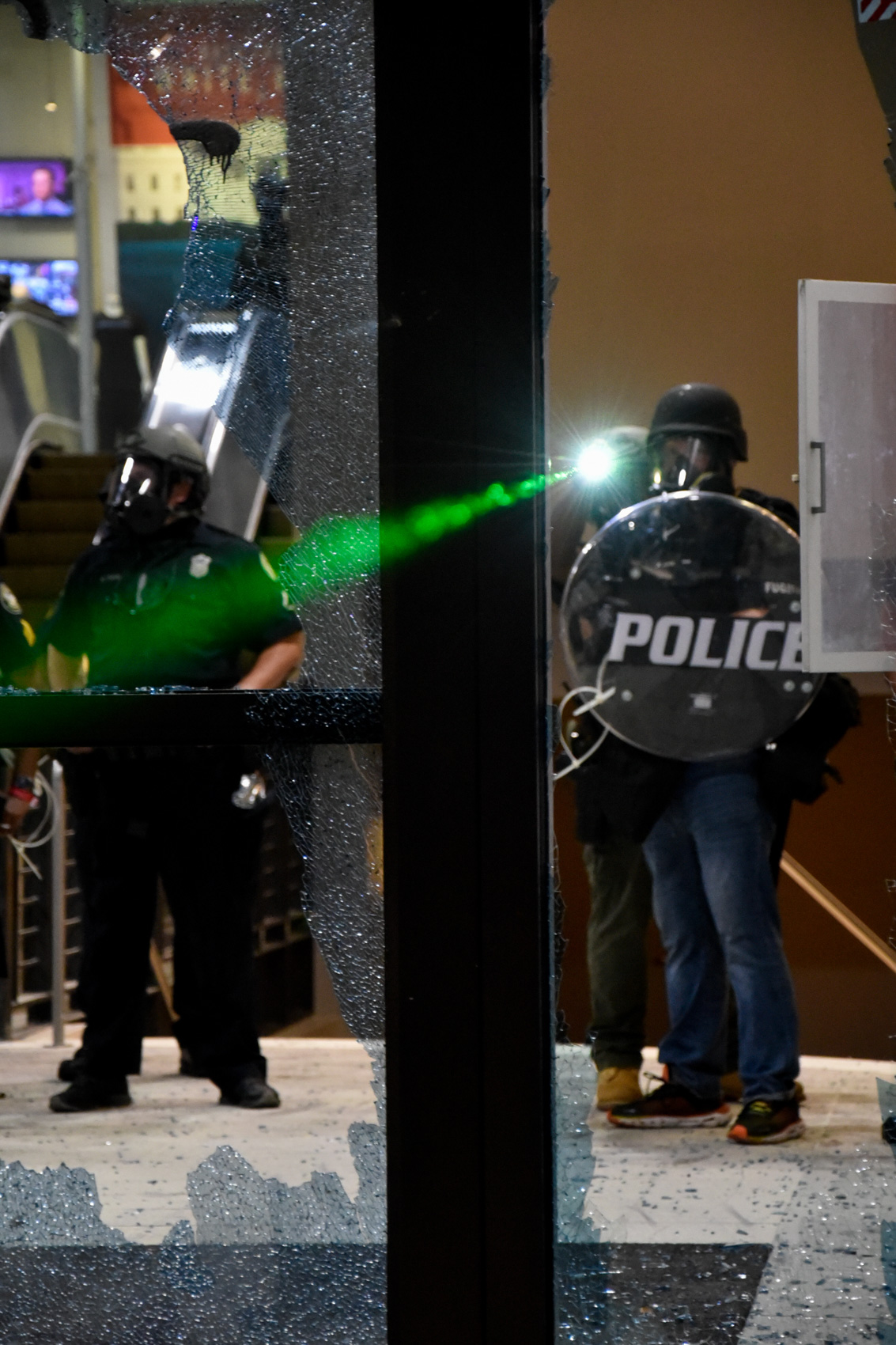 police officer holds up riot shield while another points a green laser