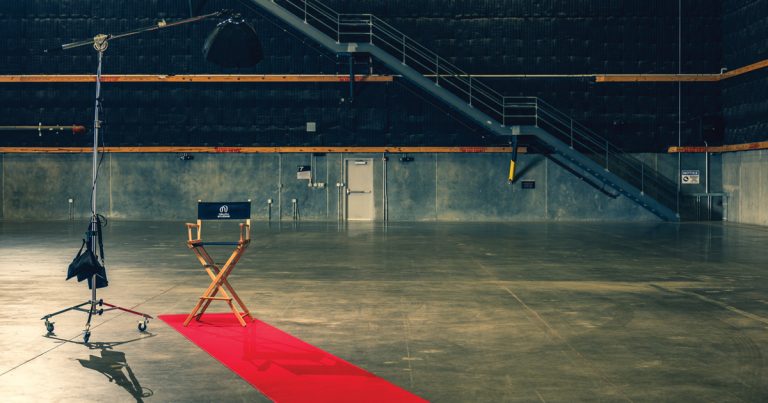 A directors chair at the end of a red carpet in an empty sound stage