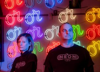 Vyvyan Hughes and Craig Weido in front of a wall of neon signs