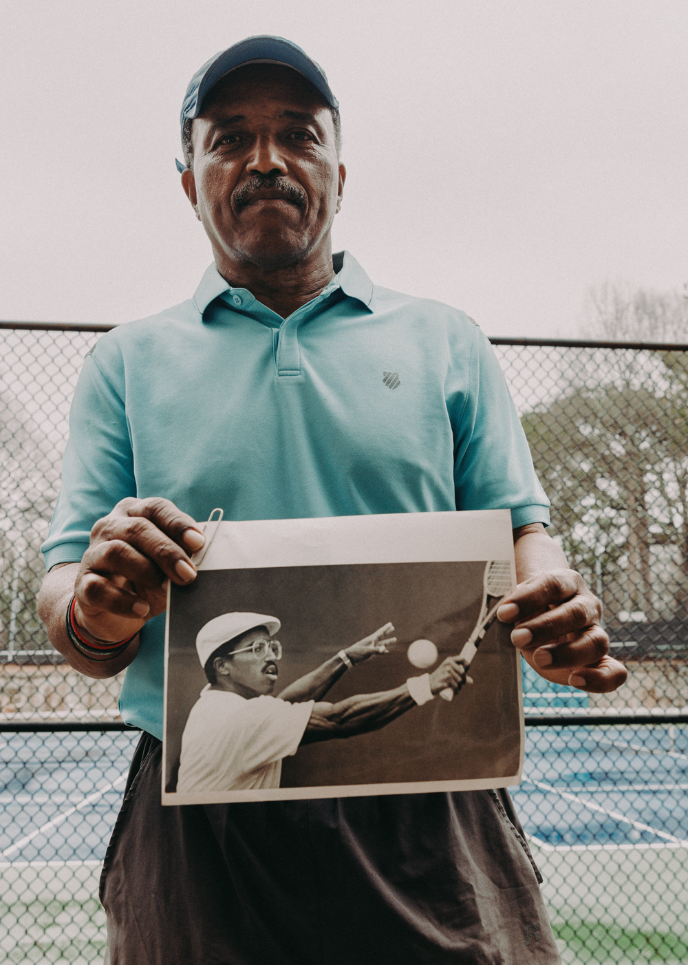 Horace Reid holds a black and white photo of himself playing tennis when he was younger