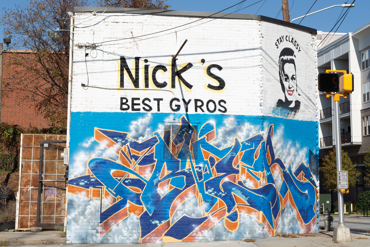 The outside of Nick's Food To Go building, with blue graffiti words and a graffiti women with the words "Stay classy" above her
