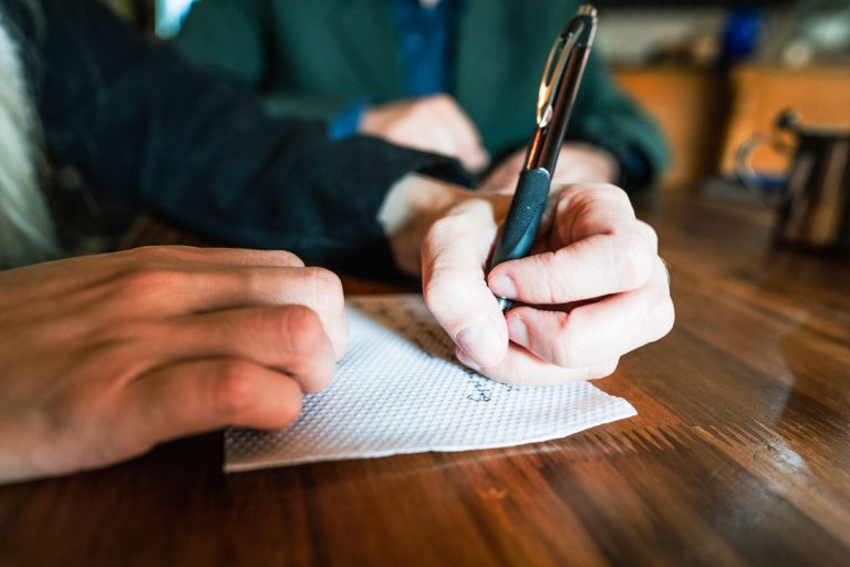 A man in a coffee shop writing on a napkin with a pen