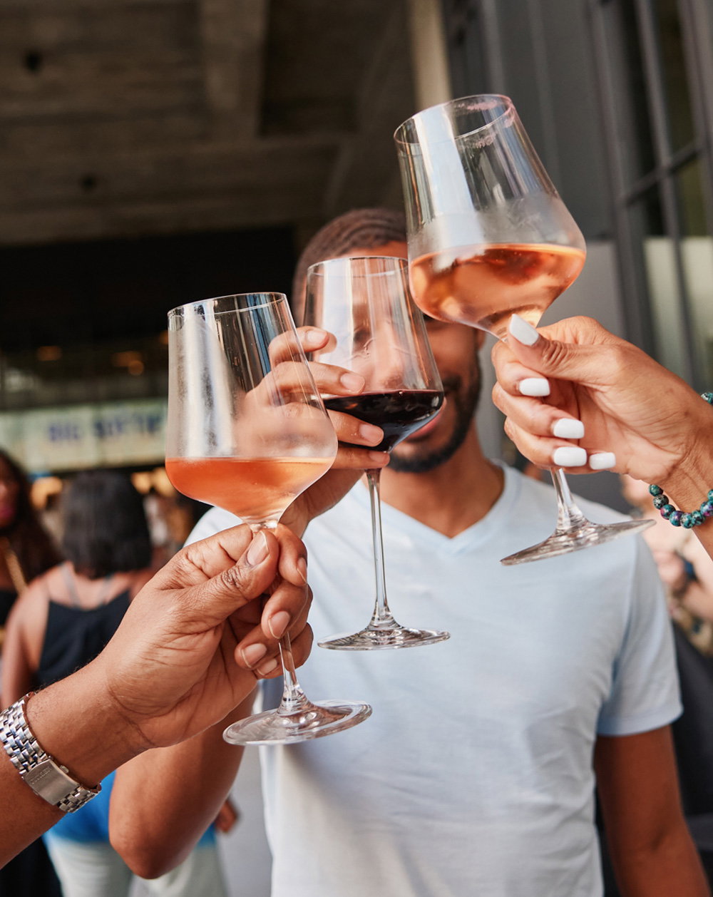 Three hands hold glasses of wine as they clink together