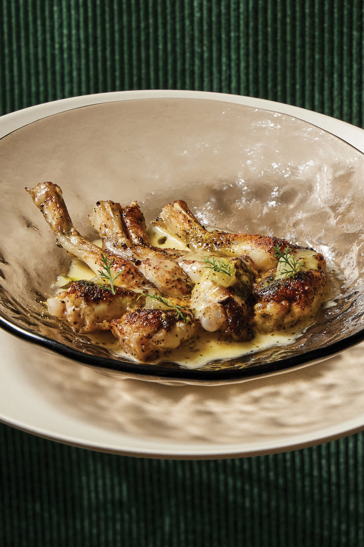 Lemon pepper wet frog legs sit in a bowl on a plate