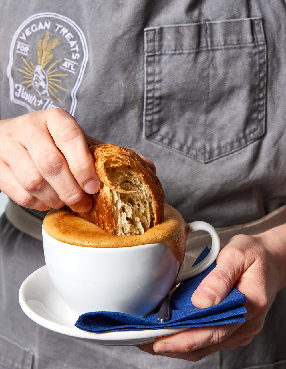 a flaky croissant being dipped into a cup of foamy coffee