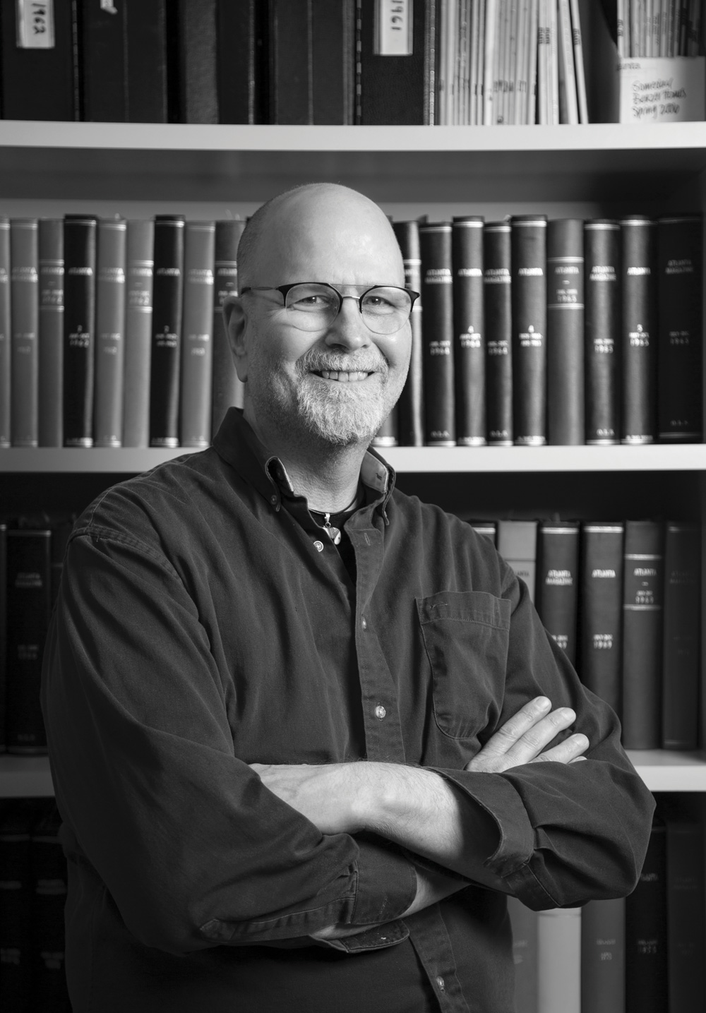 A black and white headshot of Scott Freeman crossing his arms and smiling in front of a bookshelf