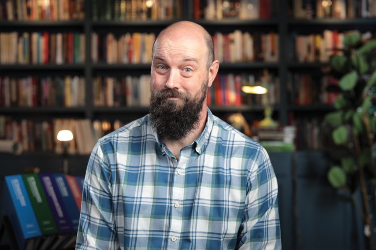 a photo of Steve Heimler wearing a blue and white plaid shirt, sitting in the space where he usually records his youtube videos