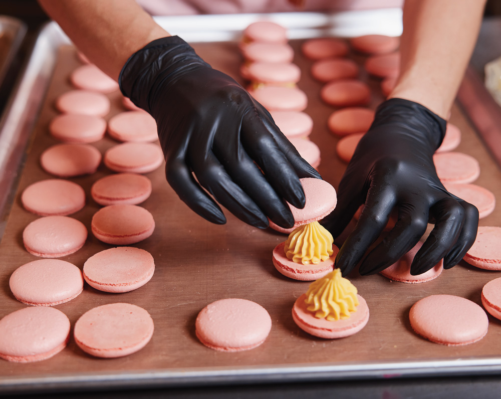 a pair of hands with black gloves assemble pink macroons from a baking sheet