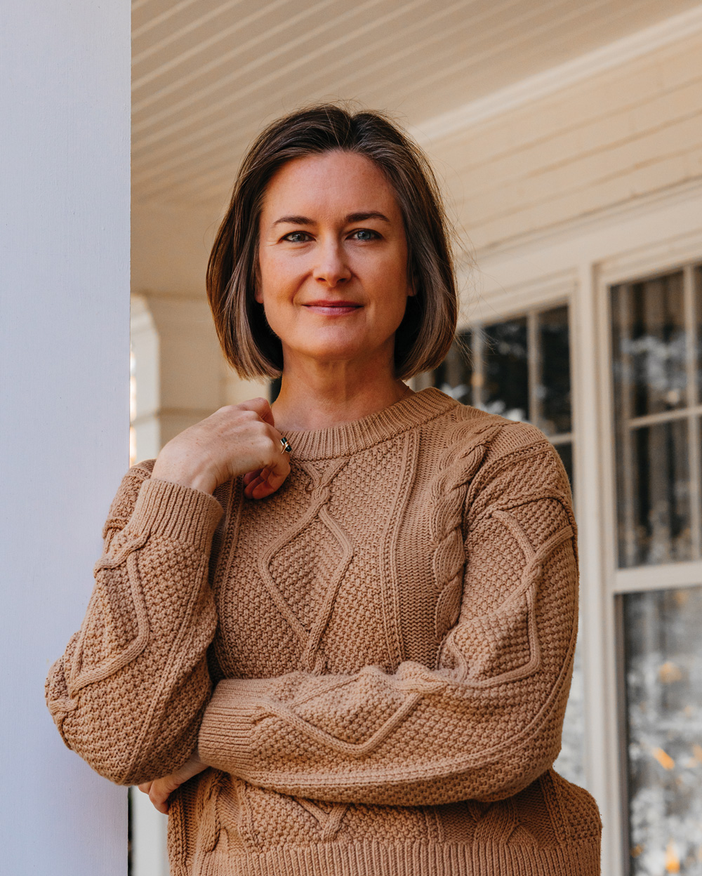 Katherine Wilkinson smiles as she wears a tan colored cable knit sweater