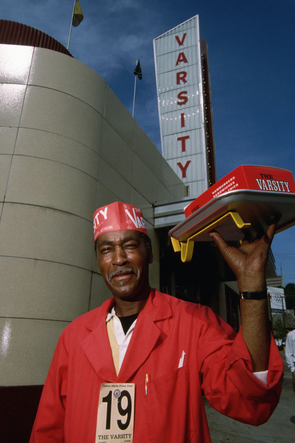 A man wearing a Varsity hat holds a tray of food outside the Varsity