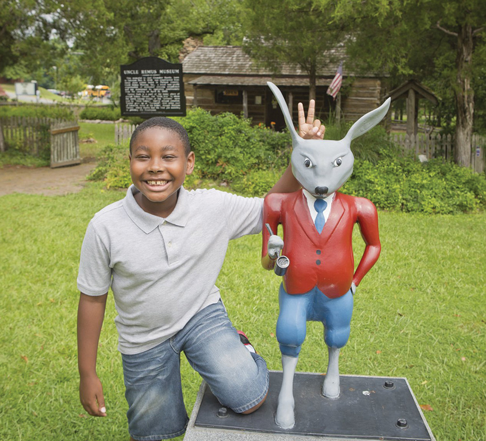 a boy smiles next to a rabit sculpture