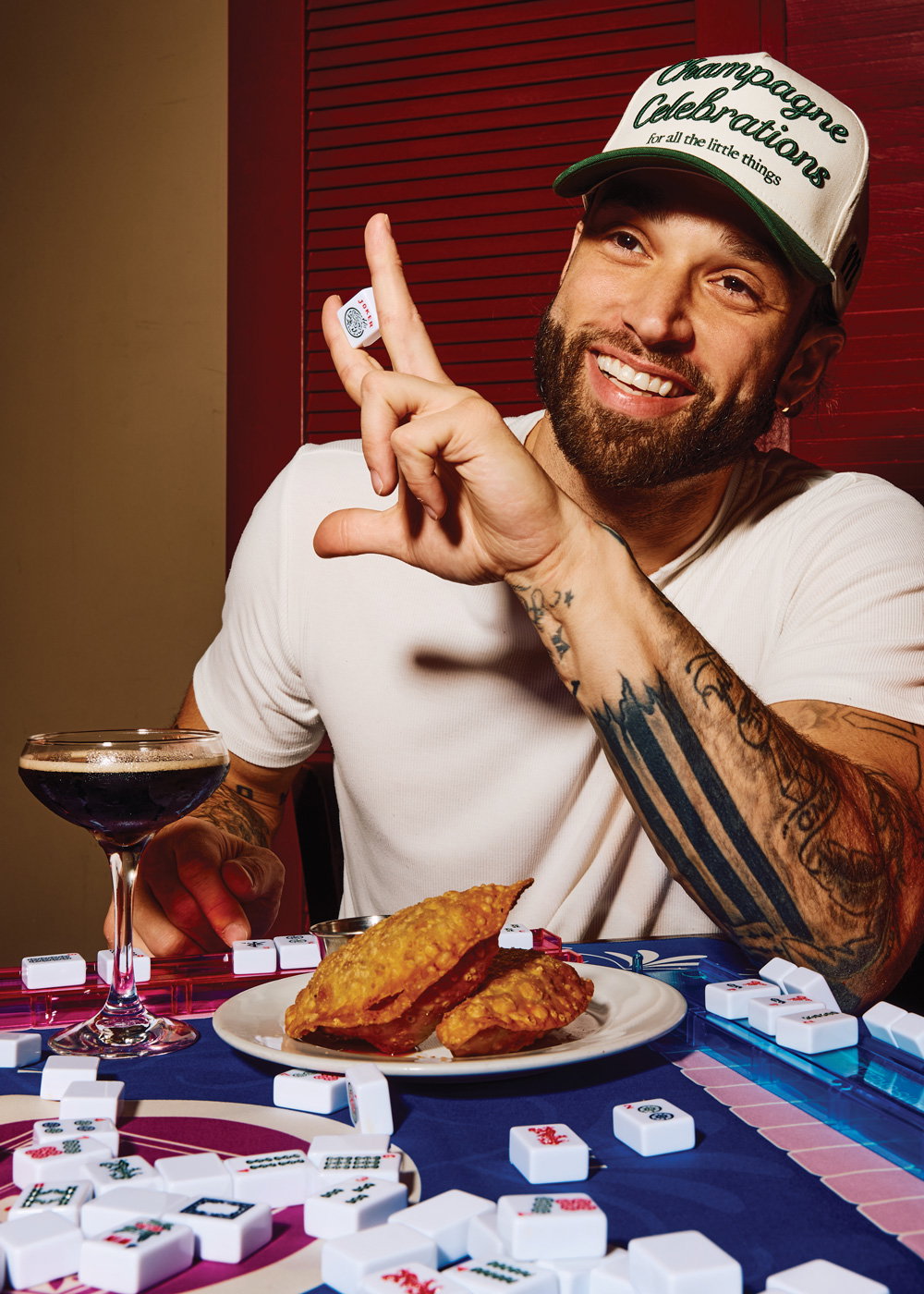 a man holds a Mahjong tile in his hand while enjoying an espresso martini and barbacoa empanadas