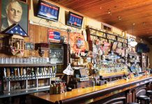 the bar at Manuel's Tavern, adorned with many glasses, drinks, and oak wood ceilings