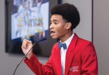 Isaiah Stephens at Harvard’s summer debate program, wearing a red blazer and speaking into a mic
