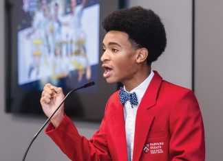 Isaiah Stephens at Harvard’s summer debate program, wearing a red blazer and speaking into a mic