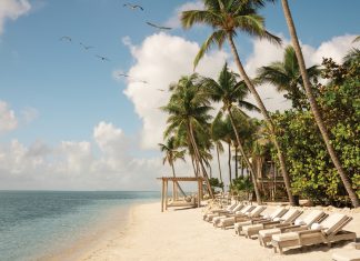 A beach shore in Little Palm Island with chaise lounge chairs and a pergola