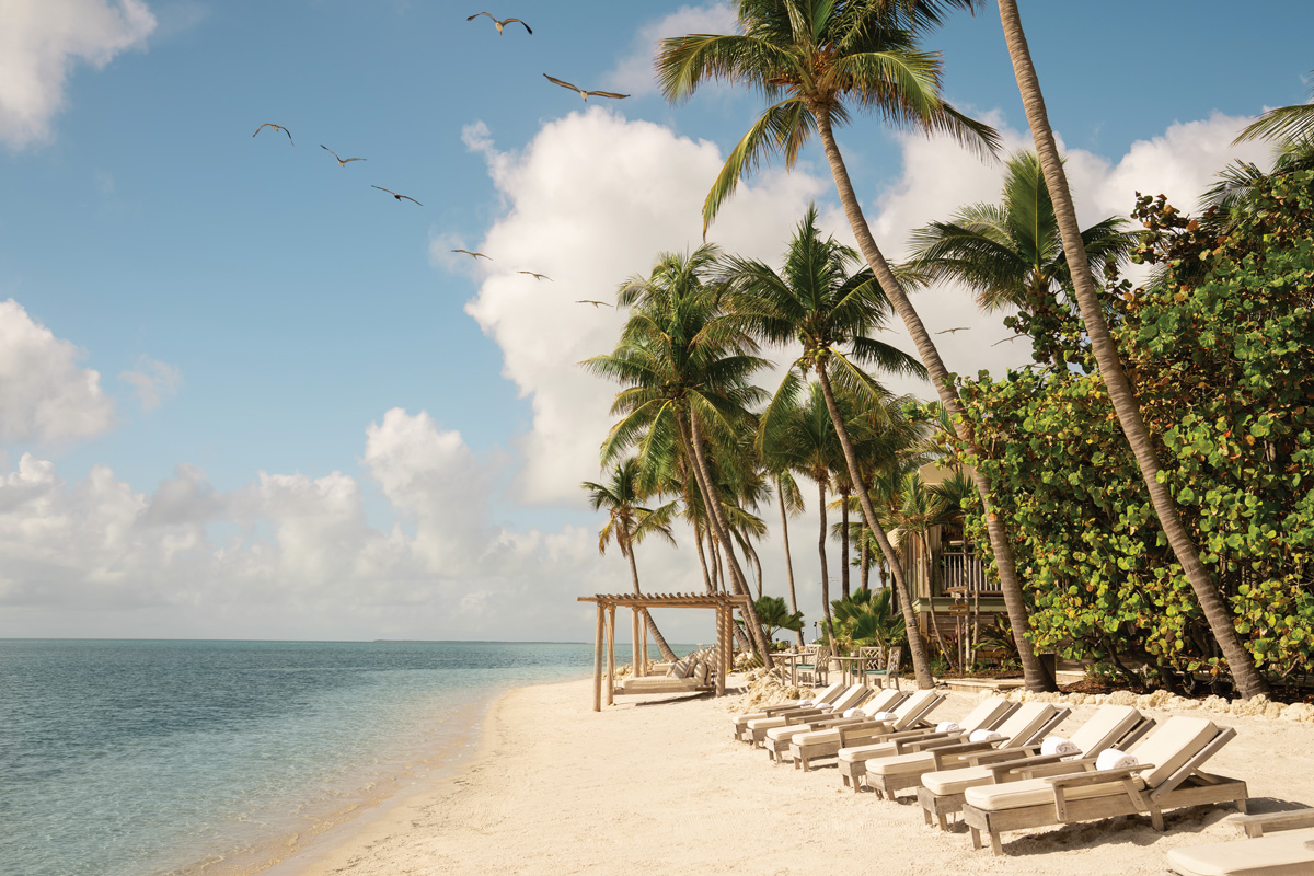 A beach shore in Little Palm Island with chaise lounge chairs and a pergola
