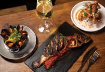 Grilled branzino with stewed tomatoes and mussels next to chicken wings over waffles
