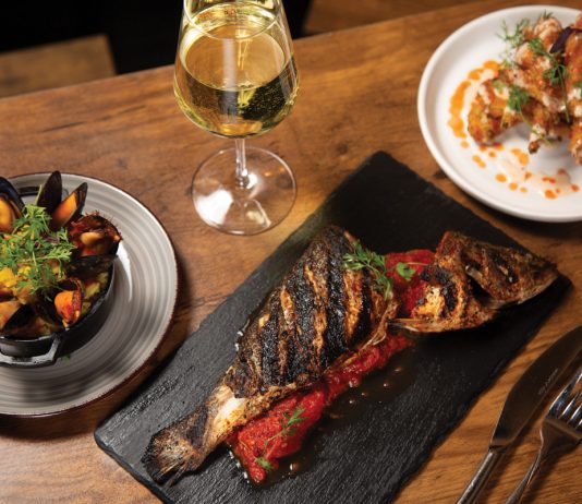 Grilled branzino with stewed tomatoes and mussels next to chicken wings over waffles