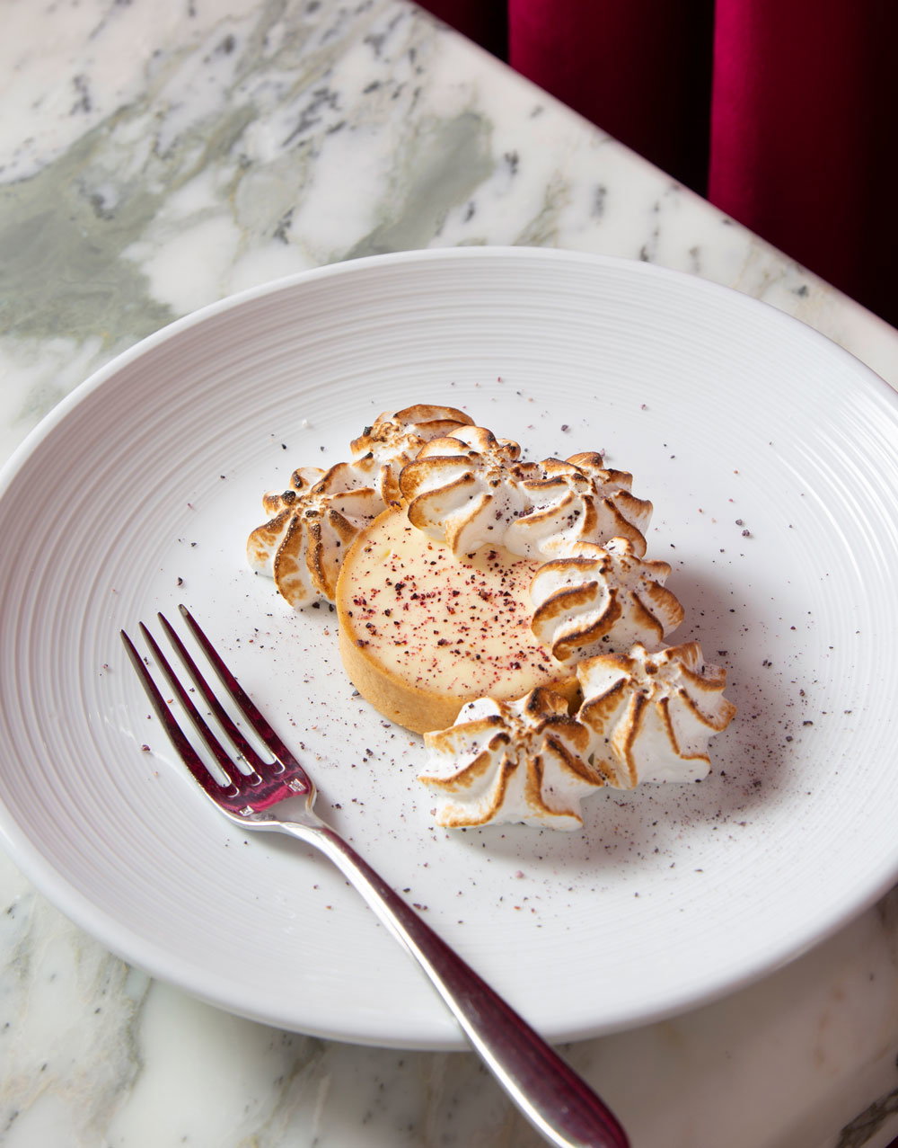 A lemon tart on a plate next to a fork