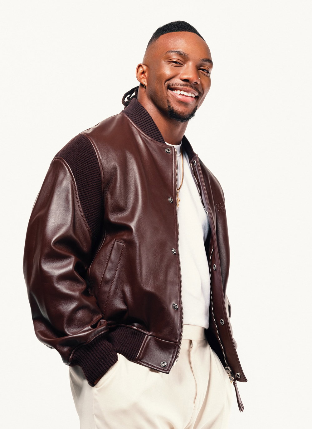Bijan Robinson wears a brown leather jacket with a white tshirt and pants