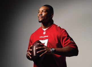 Bijan Robinson wears his red Falcons jersey while holding a football against a gradient black and white backdrop