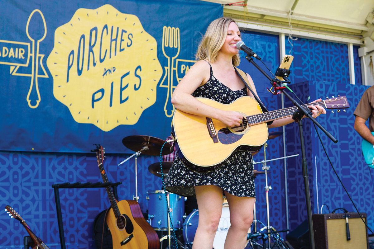a woman sings and plays guitar on stsge at the Porches & Pies Festival