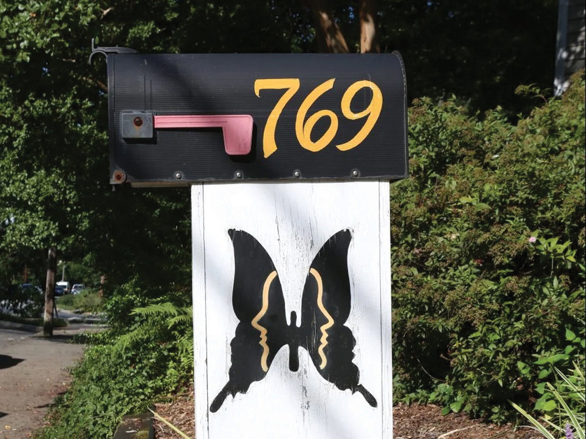 a handpainted butterfly sign below a black mailbox that reads the numbers 769