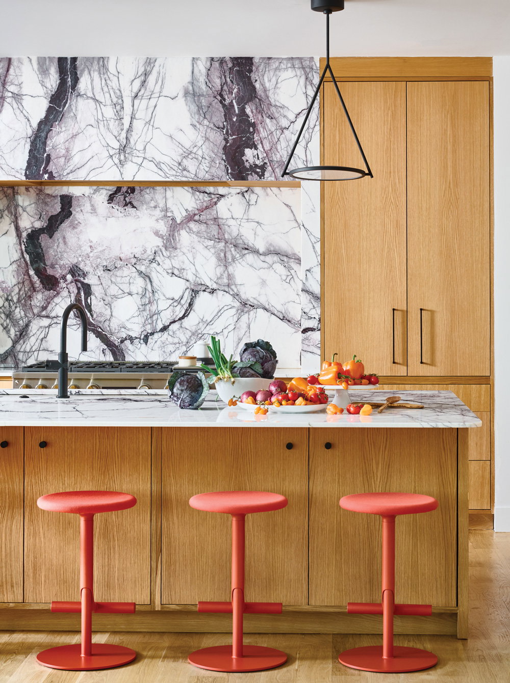 a cheerful kitchen with oak wooden cabinets and red/orange barstools