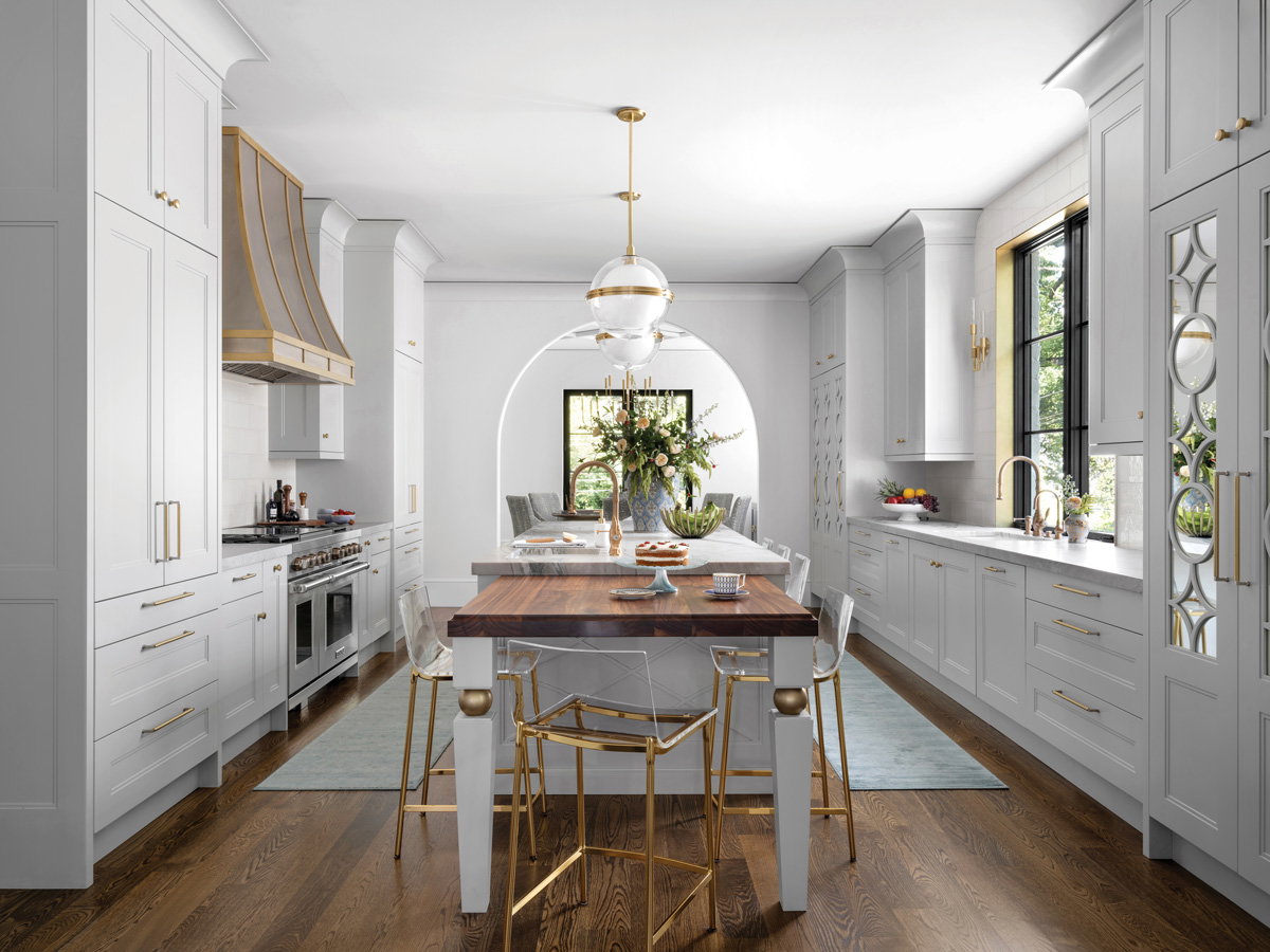 an all white kitchen with yellow gold accents and a wooden and marble kitchen island