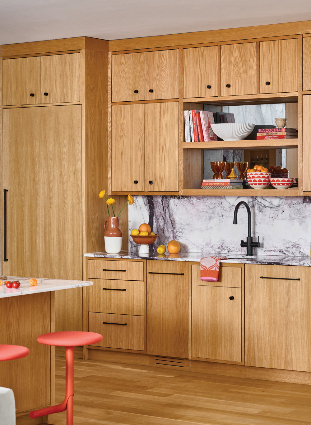 an all oak kitchen with red/orange barstools and marble backsplash walls