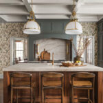 a rustic kitchen with a marble and wooden island in the middle and two overhead lamps above it