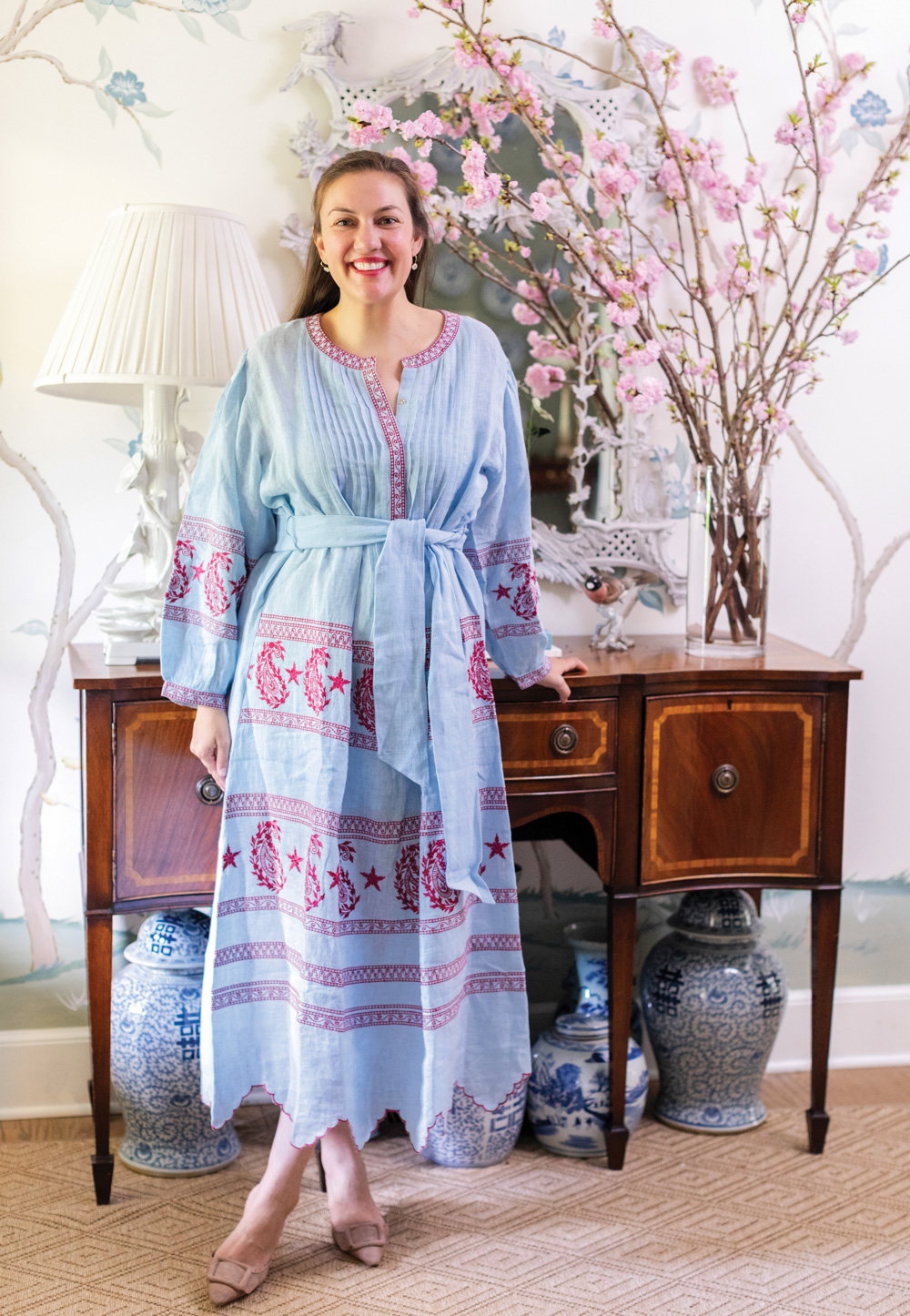 Elizabeth Cook stands in front of a woden console table with bright light pink cherry blossom flowers atop it.