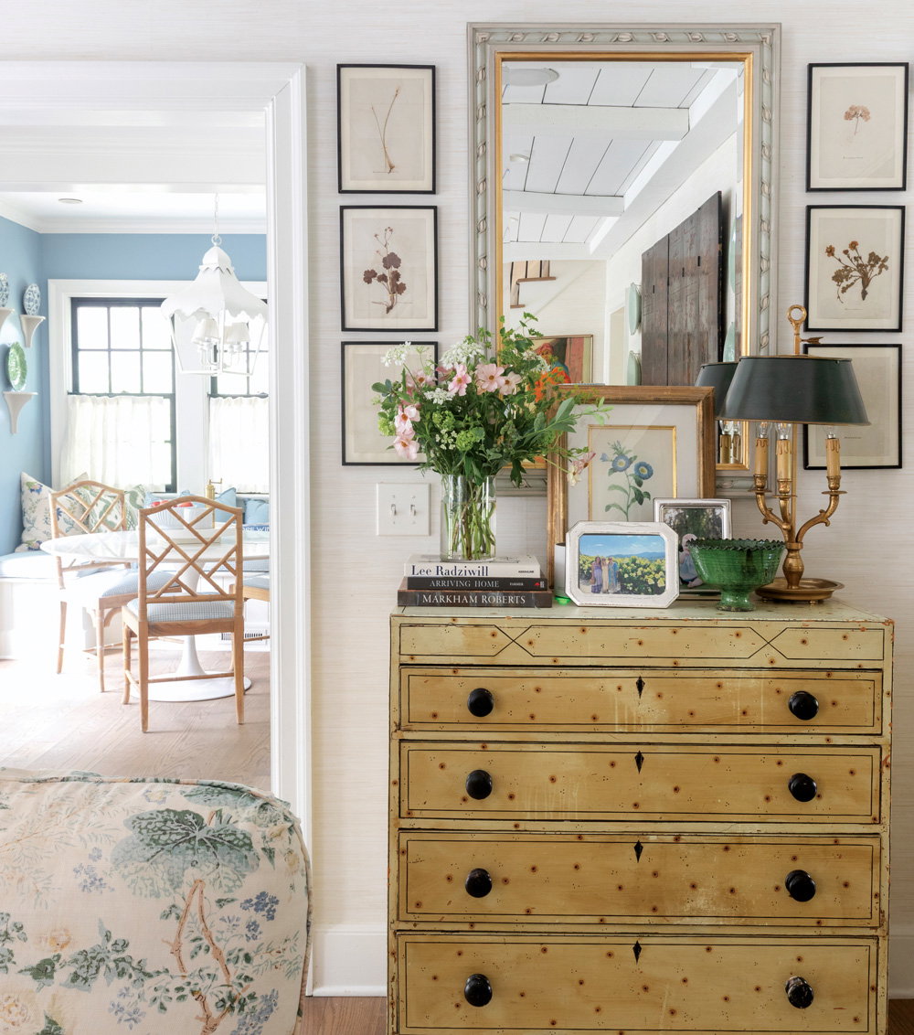 a room with a mirror and artworks around it, and a doorframe leading to another sitting room with blue walls and chairs