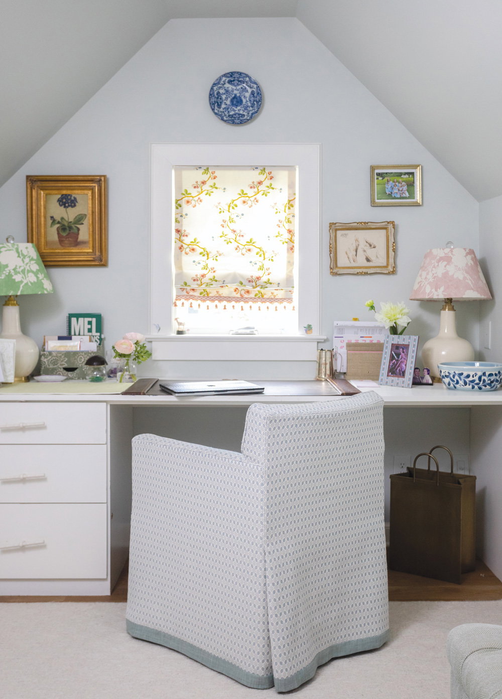 a top floor room with caved ceilings, a desk and chair pushed against the wall next to the window