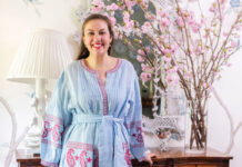 Elizabeth Cook stands in front of a woden console table with bright light pink cherry blossom flowers atop it.