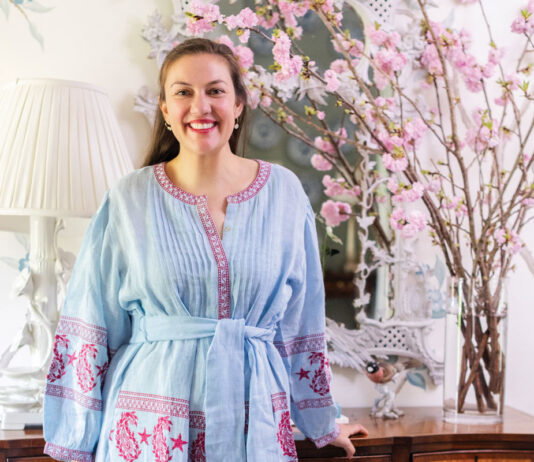 Elizabeth Cook stands in front of a woden console table with bright light pink cherry blossom flowers atop it.