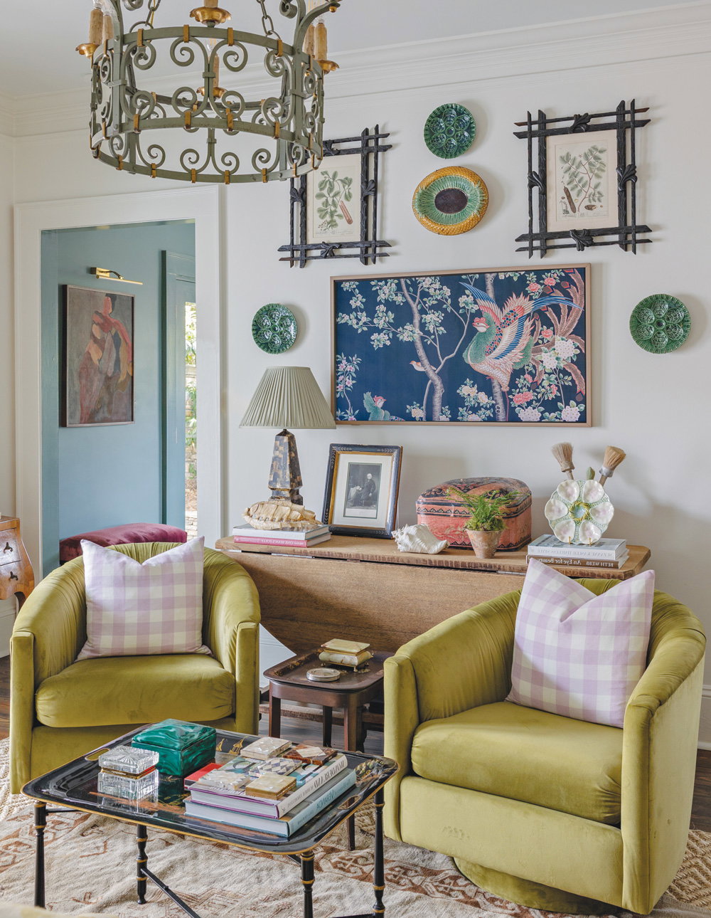 two green chairs in a room with an array of hunt artwork and an eclectic pendant lamp