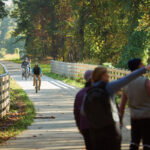6 Atlanta Neighborhoods Where Community is Key: Smyrna Three people point and look at the trees while two bike riders ride down the Silver Comet Trail