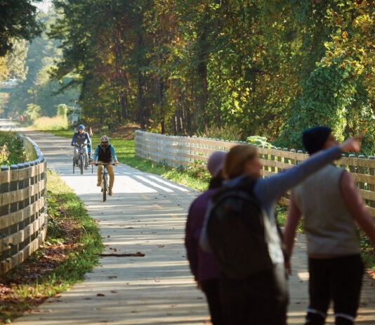 6 Atlanta Neighborhoods Where Community is Key: Smyrna Three people point and look at the trees while two bike riders ride down the Silver Comet Trail