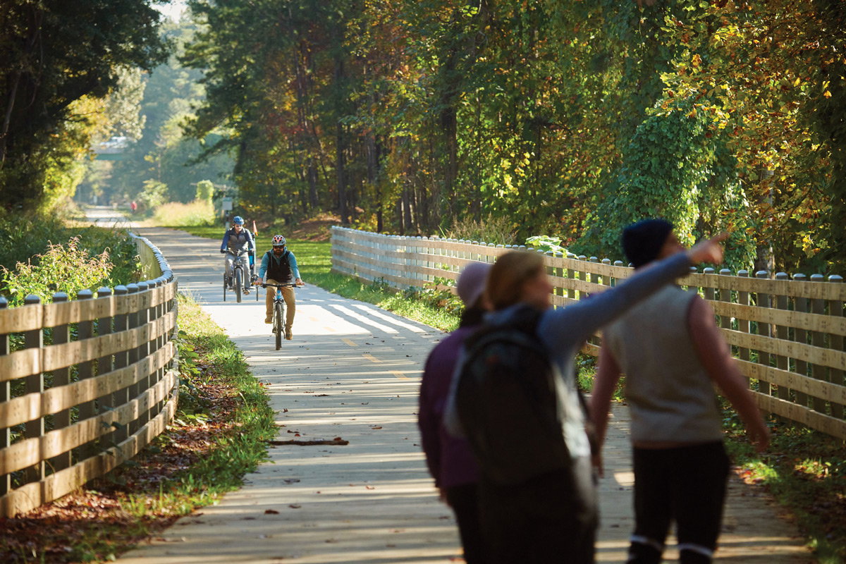 Three people point and look at the trees while two bike riders ride down the Silver Comet Trail