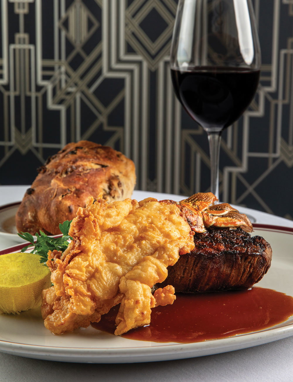 A fried lobster tail on top of a steak with a glass of wine in the background