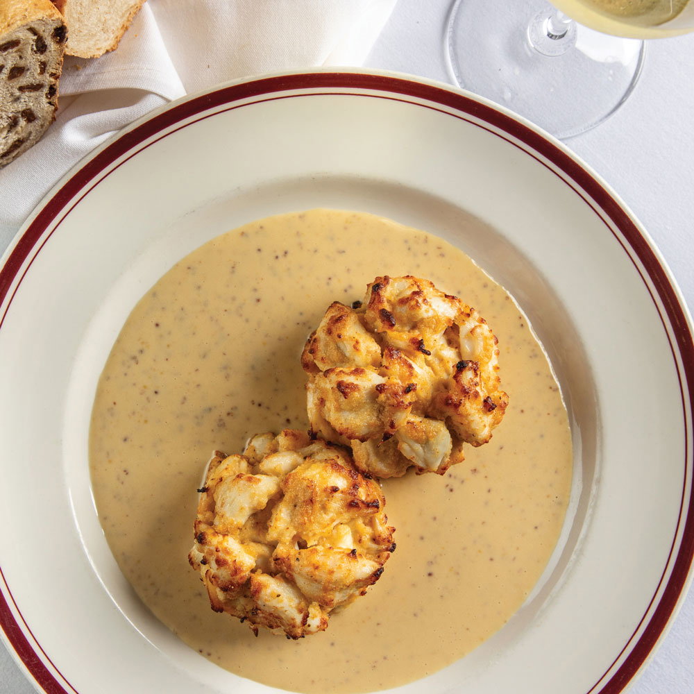 Two Maryland crab cakes in a bowl of sauce