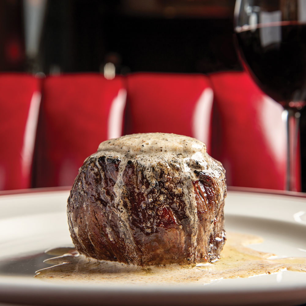 A juicy steak on a plate with a glass of wine in the background