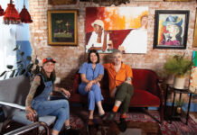 three people sit in mismatch couches against a brick wall with an array of paintings inside Last Dance