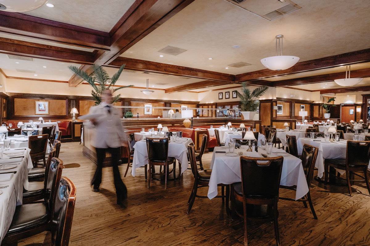 A server walks through an empty McKendrick's dining room with white table cloths