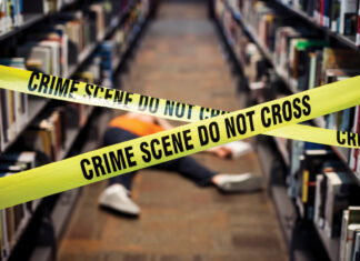 a person laid on the floor between two book isles is blocked off by yellow crime scene tape