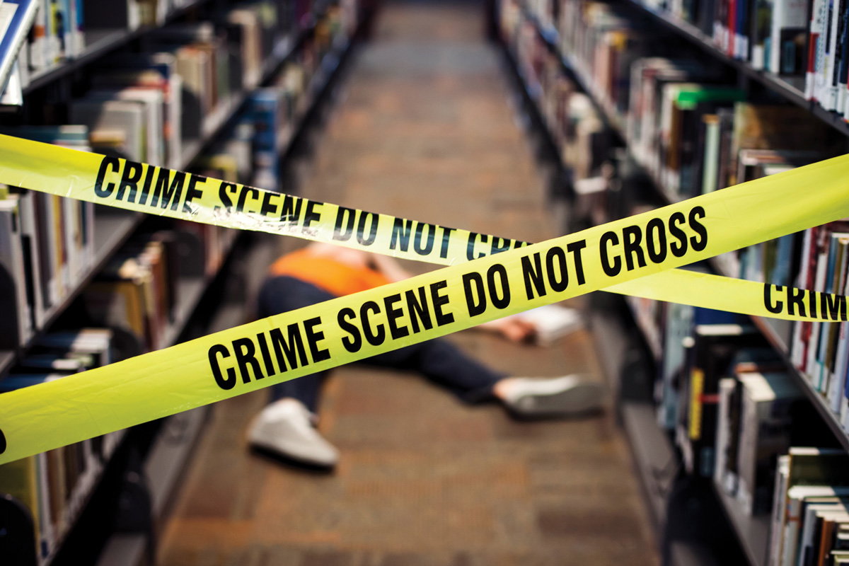 a person laid on the floor between two book isles is blocked off by yellow crime scene tape